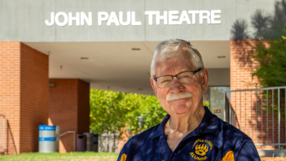 Marty Manning stands in his Phoenix College alumni shirt in front of John Paul Theatre