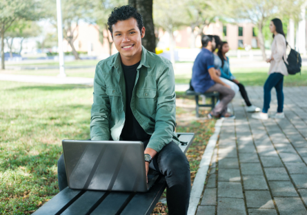 student sitting outside on campus in front of a laptop