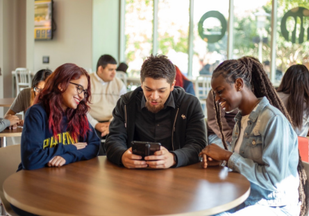 Three Phoenix College students sit around a table looking at a social media post on an ipad.