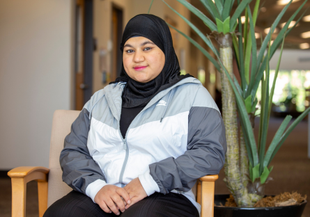 Sally Alsigab sit in a chair on the second floor of Fannin Library. She is wearing a black hijab and white and gray athletic jacket. 