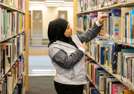 Phoenix College student Sally Alsigab looks at books on the shelf at Fannin Library. 